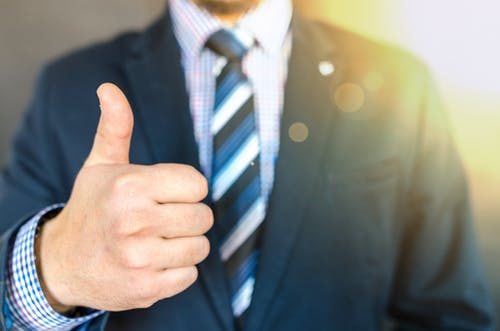 man in blue suit and striped tie giving a thumbs up