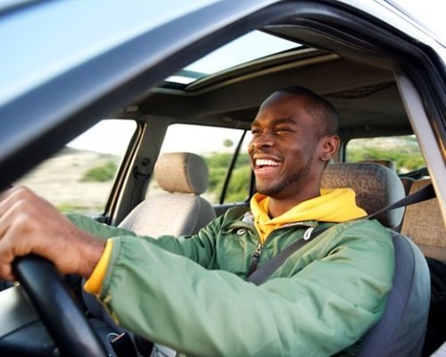 Black man in a green jacket driving a car and smiling